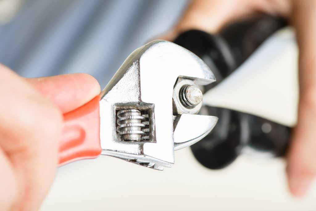 Appliance repair technican fastens a nut on a bolt using a red-handled wrench